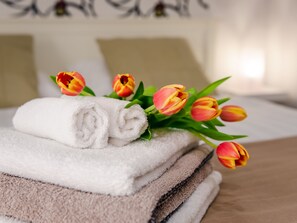 A stack of neatly folded towels and a bouquet of tulips on a bed. - Casa Montana-Mokka Apartment (Balatonalmadi)