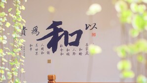 Una pared con grandes caracteres chinos y texto más pequeño, rodeada de vegetación.