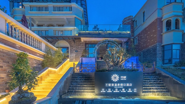 A hotel entrance with a staircase leading up to a gated entrance, surrounded by buildings and a decorative archway.