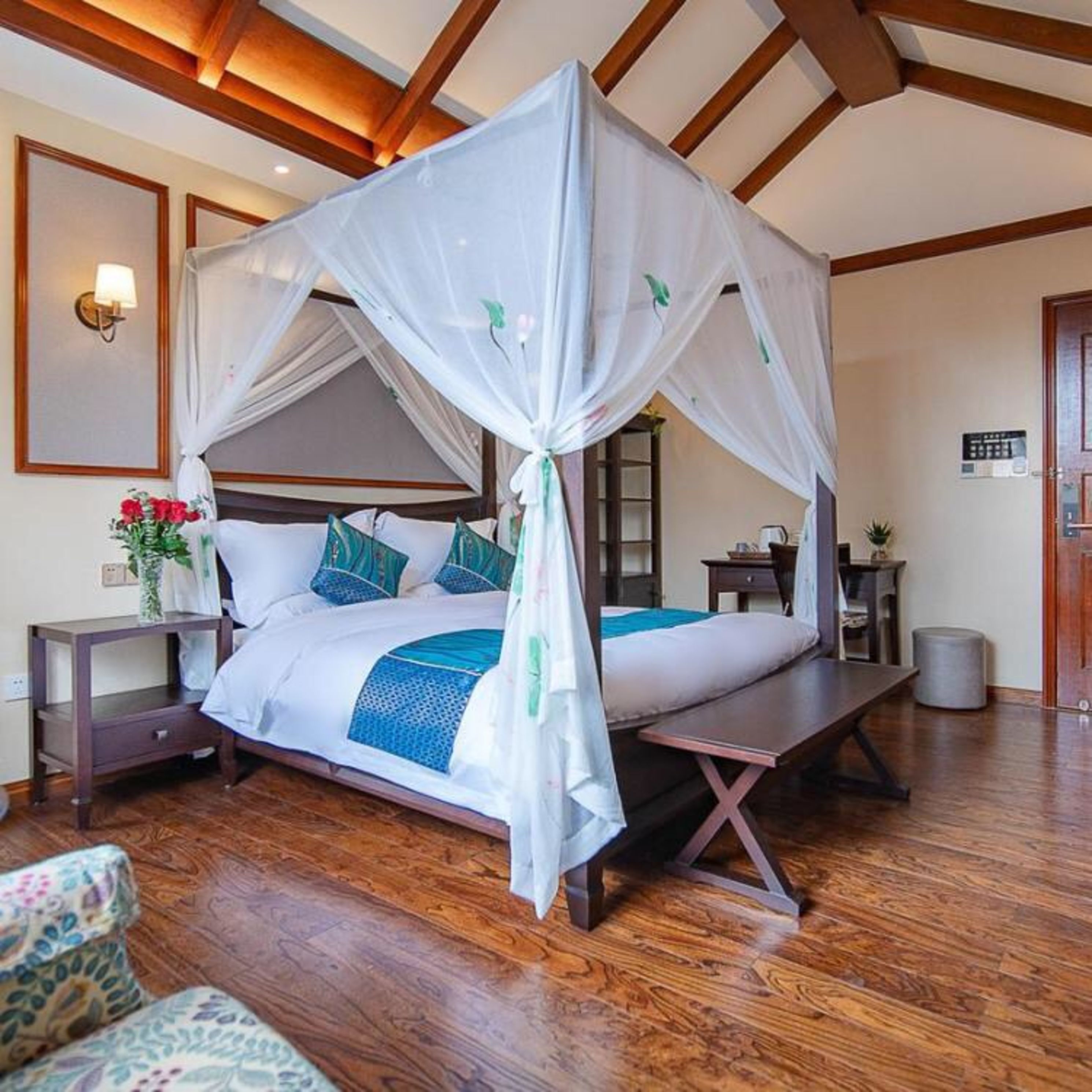 A four-poster canopy bed with a wooden frame and white bedding, a bedside table, a nightstand, and a small potted plant.