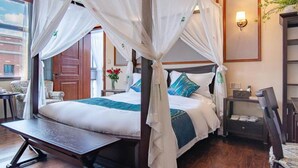 Une chambre avec un lit sous un dais, un bureau, une chaise, une table de chevet et une lampe fixée au mur.