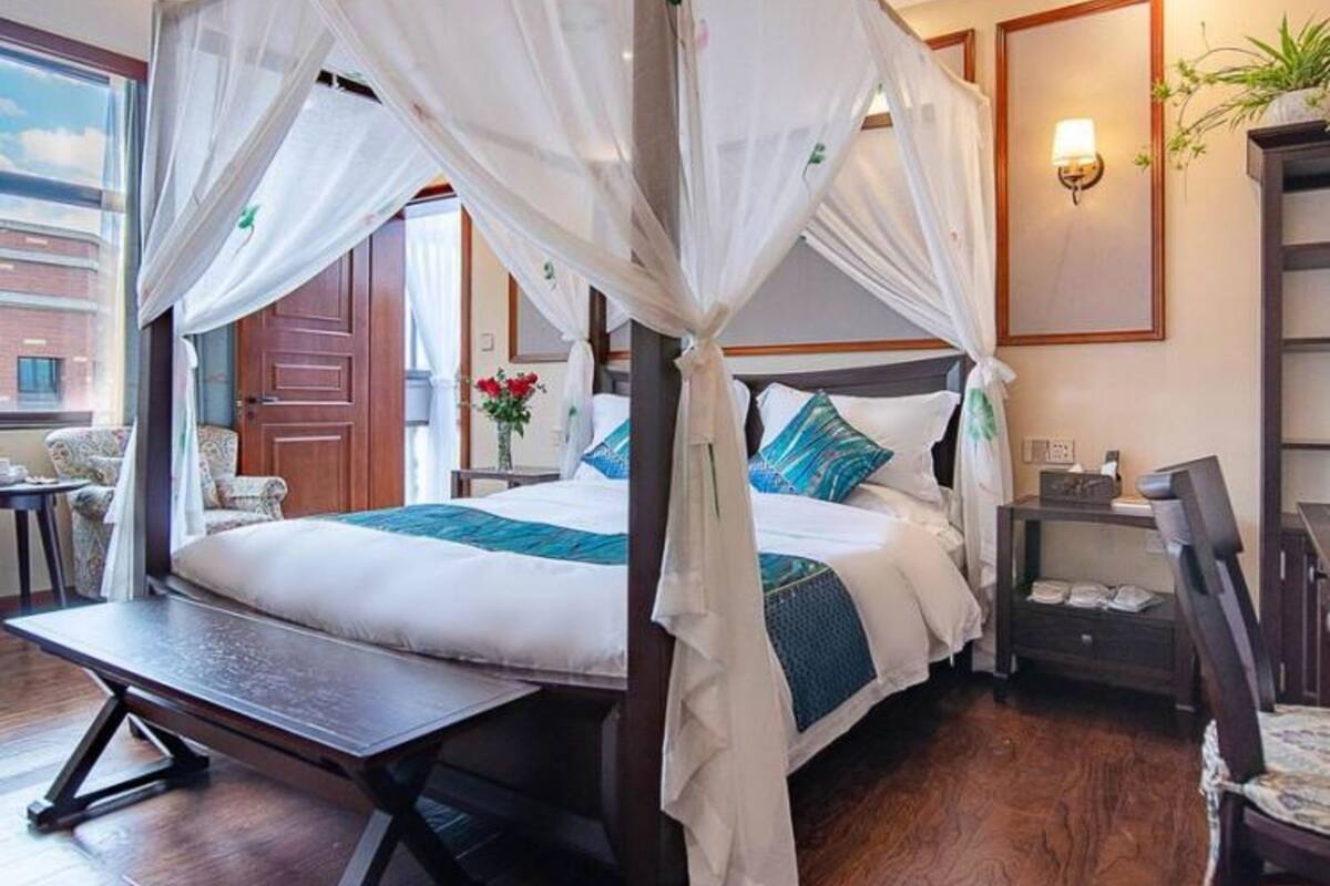 Ein Zimmer mit einem Himmelsbett, einem Schreibtisch, einem Sessel, einem Nachttisch und einer Wandlampe.