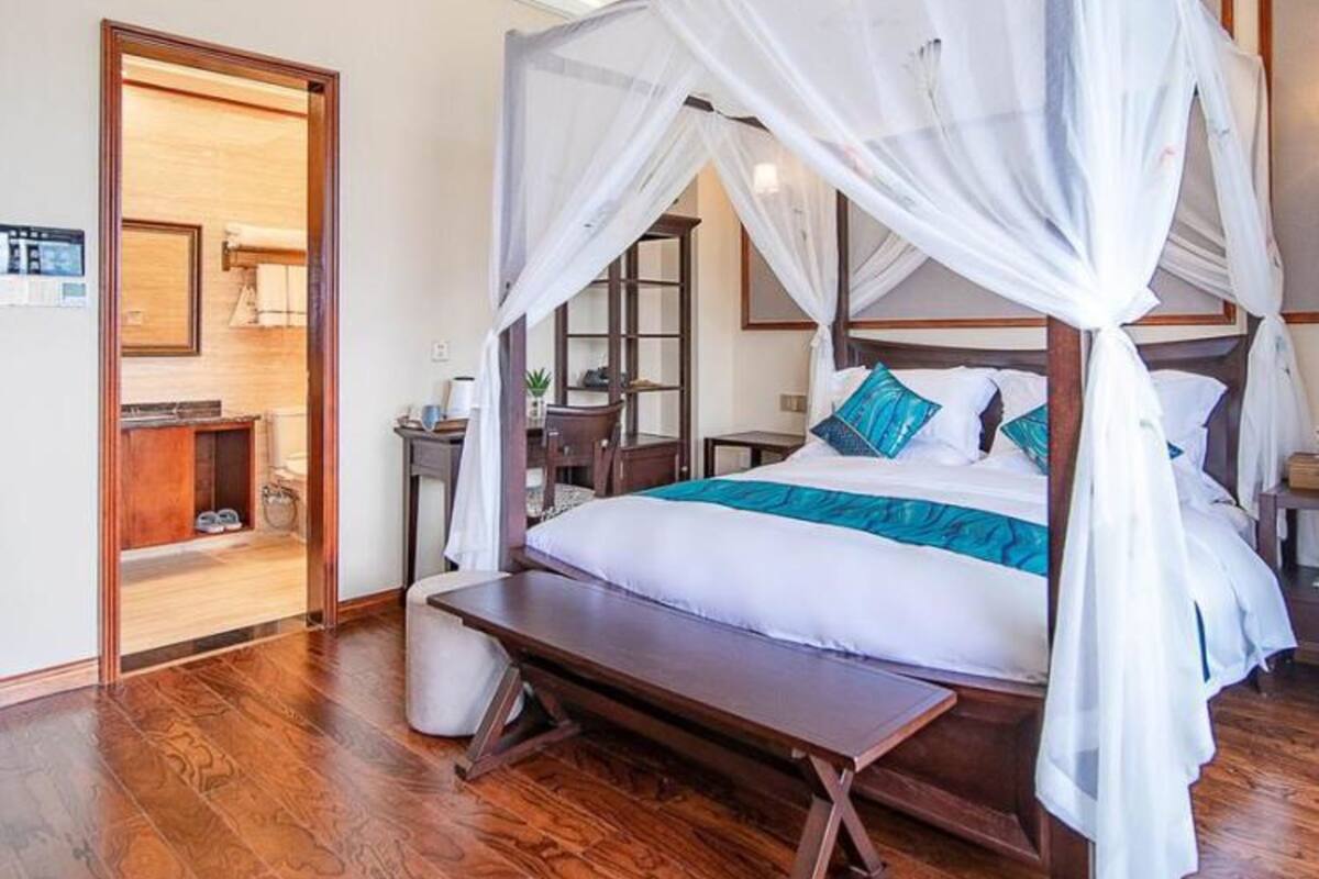 Ein Himmelsbett mit Sitzbank, Holzboden und ein Spiegel im angrenzenden Zimmer.