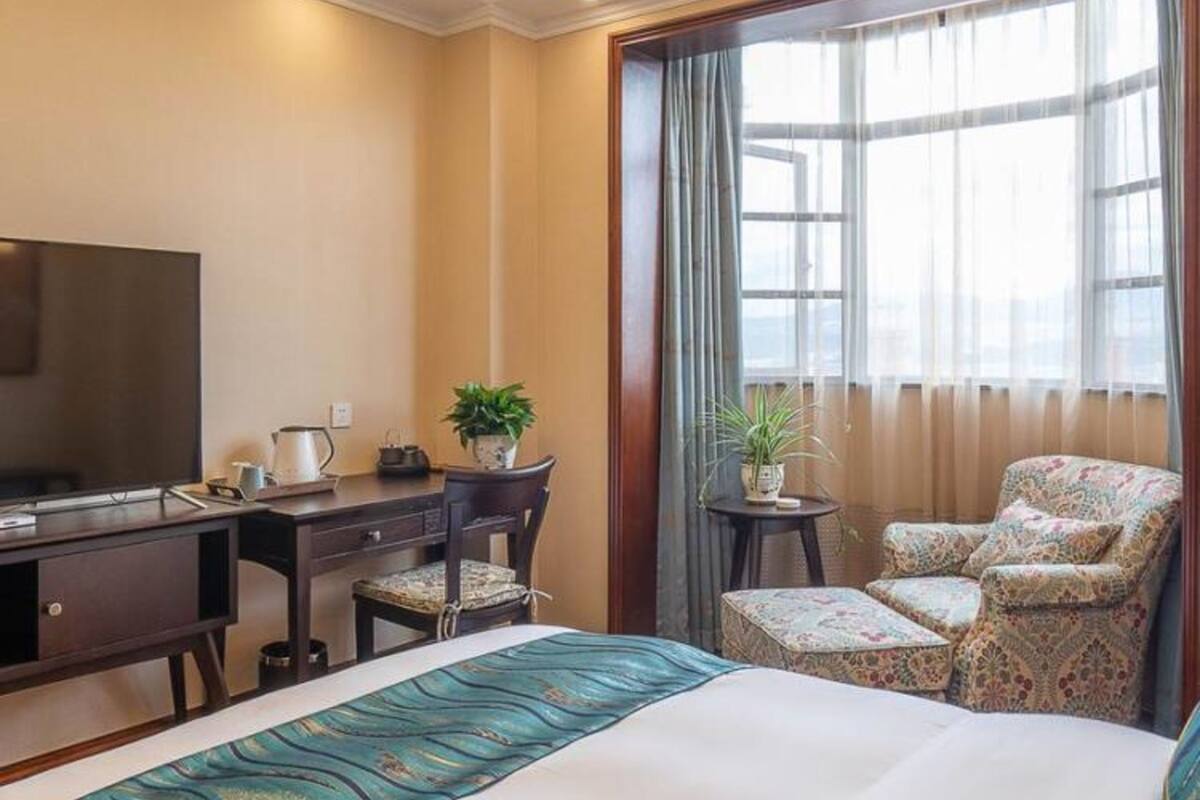 Ein Hotelzimmer mit einem Bett, einem Schreibtisch, einem Fernseher, einem Stuhl und einem fenster mit Vorhängen.