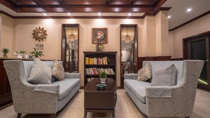 Un hall d'hôtel avec deux fauteuils à motifs, une table basse centrale et une bibliothèque remplie de livres.