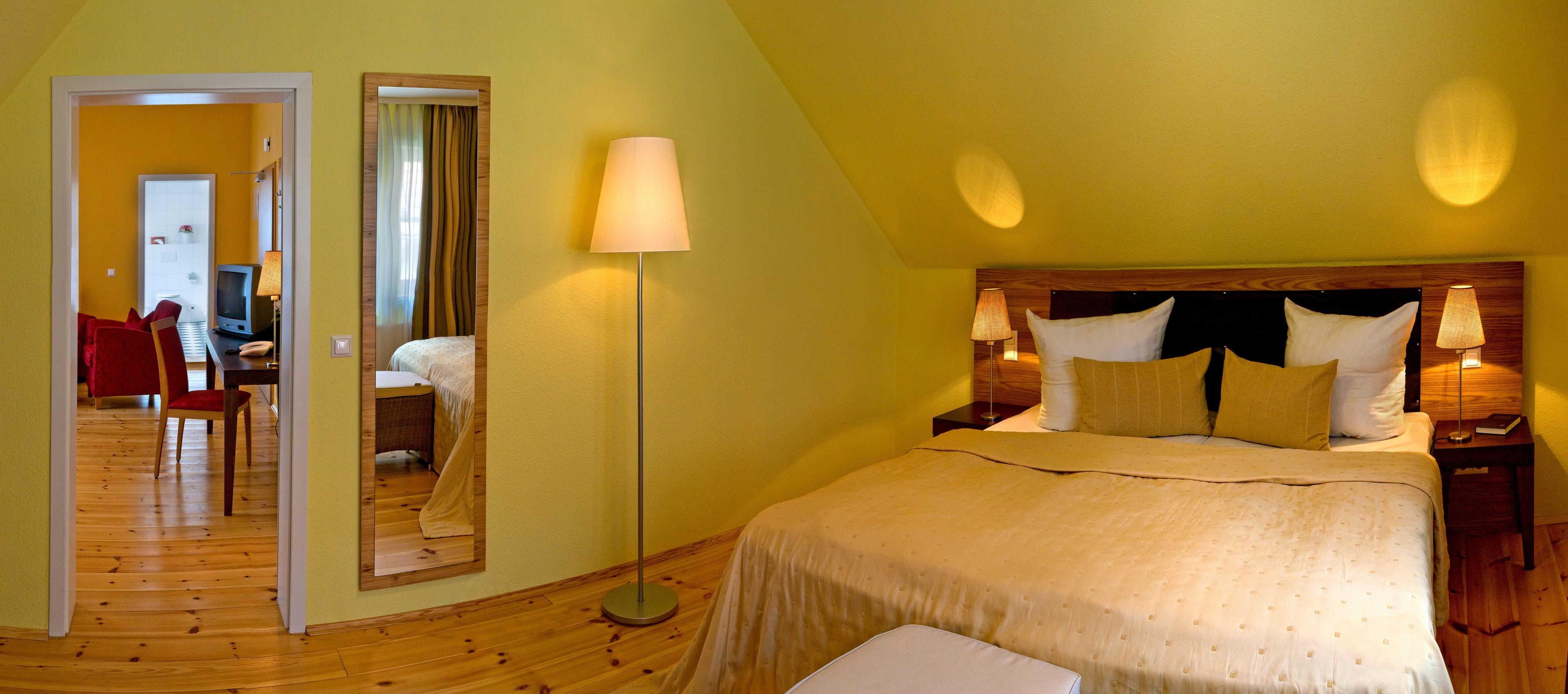 A bedroom with a bed, bedside lamps, a mirror, and a wooden floor.