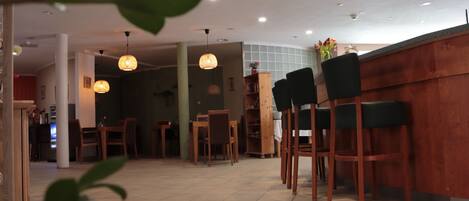A restaurant with wooden chairs and tables, a counter, and hanging pendant lights.
