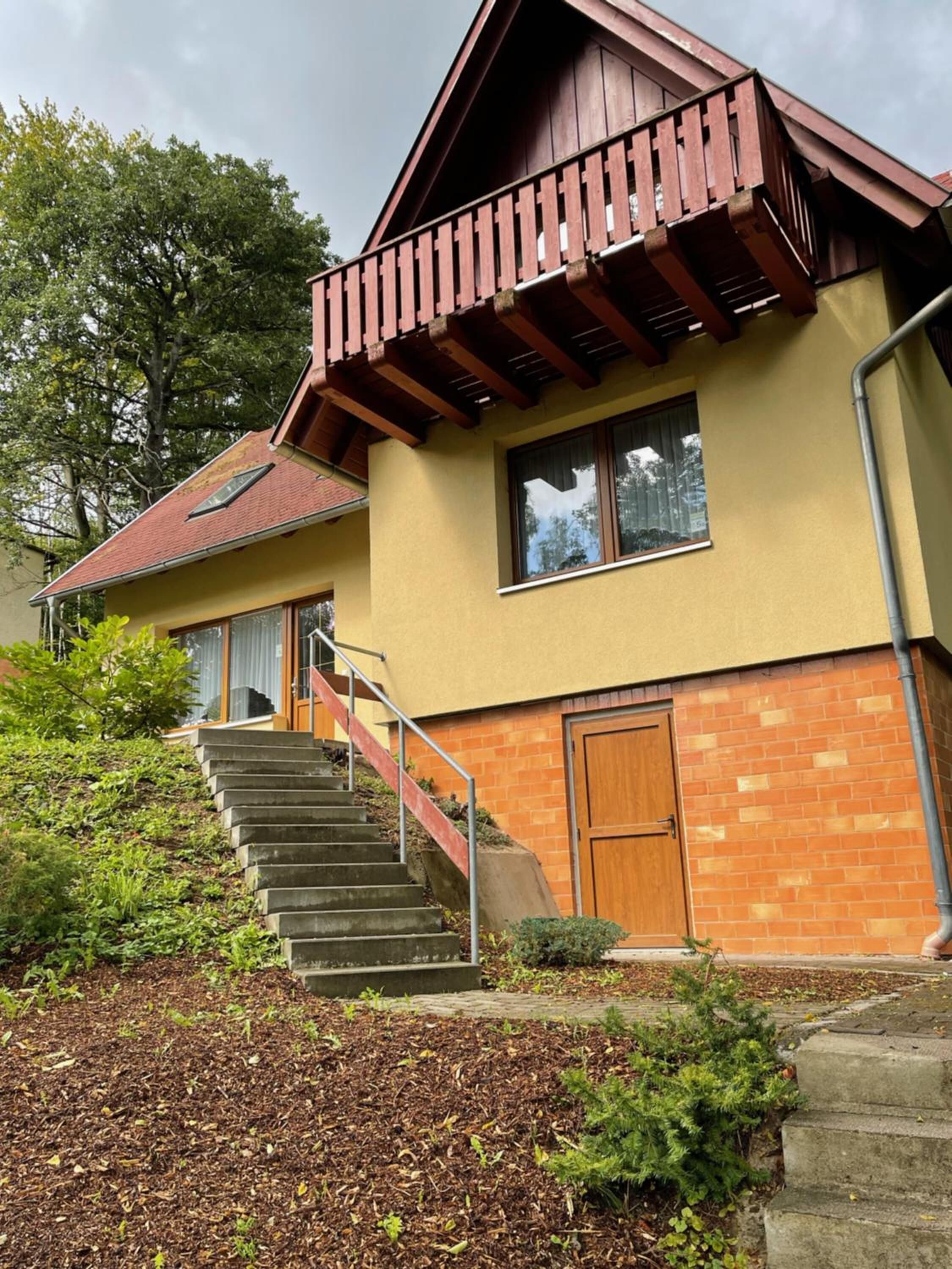 A two-story house with a wooden balcony, a brick exterior, and a set of stairs leading to the entrance.
