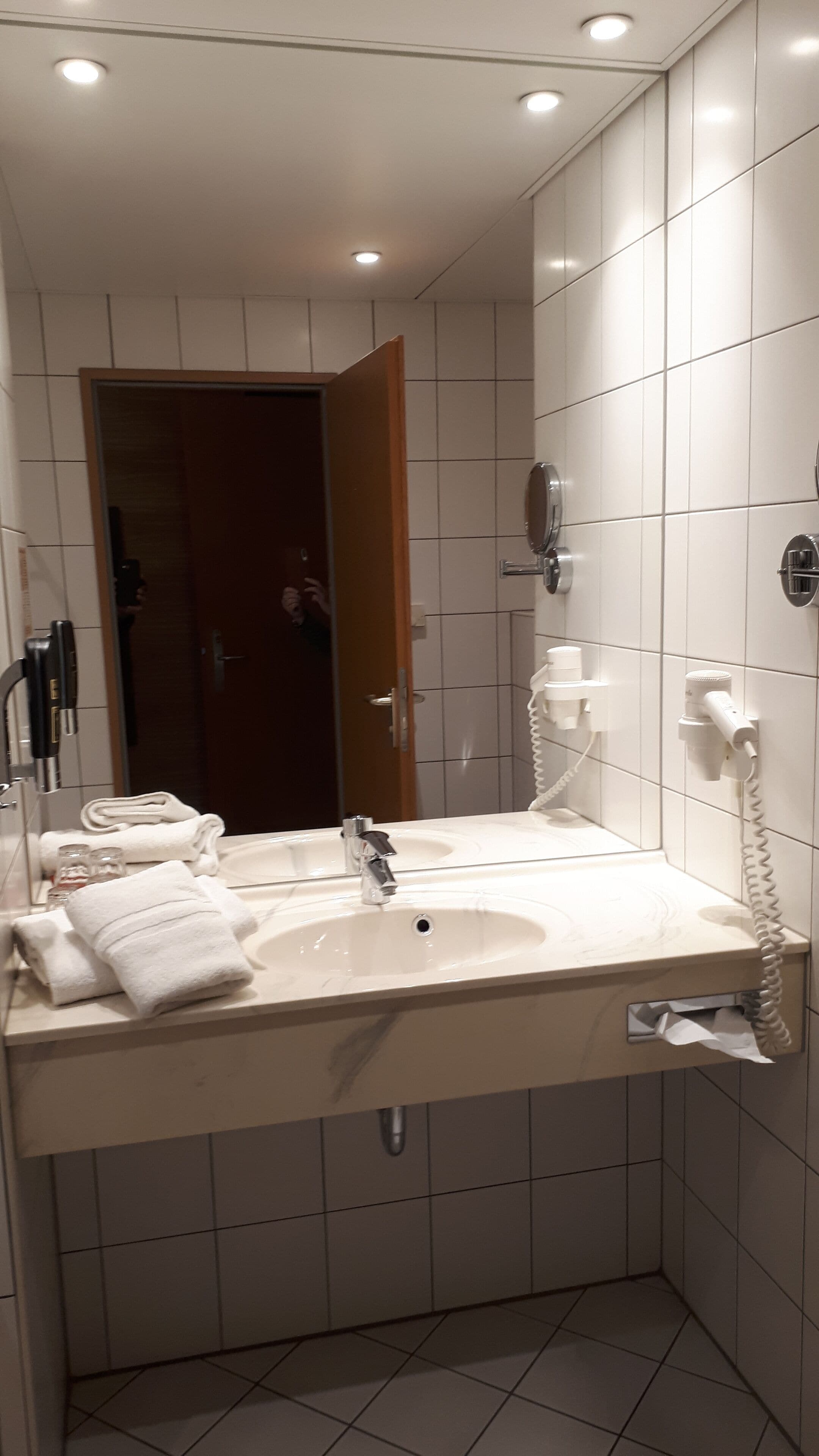 A bathroom with a sink, mirror, towel rack, and a hairdryer on the wall.