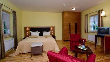 Ein Hotelzimmer mit einem großen Bett, einem roten Sessel, einem kleinen Tisch mit einer Flasche und einem Fernseher.