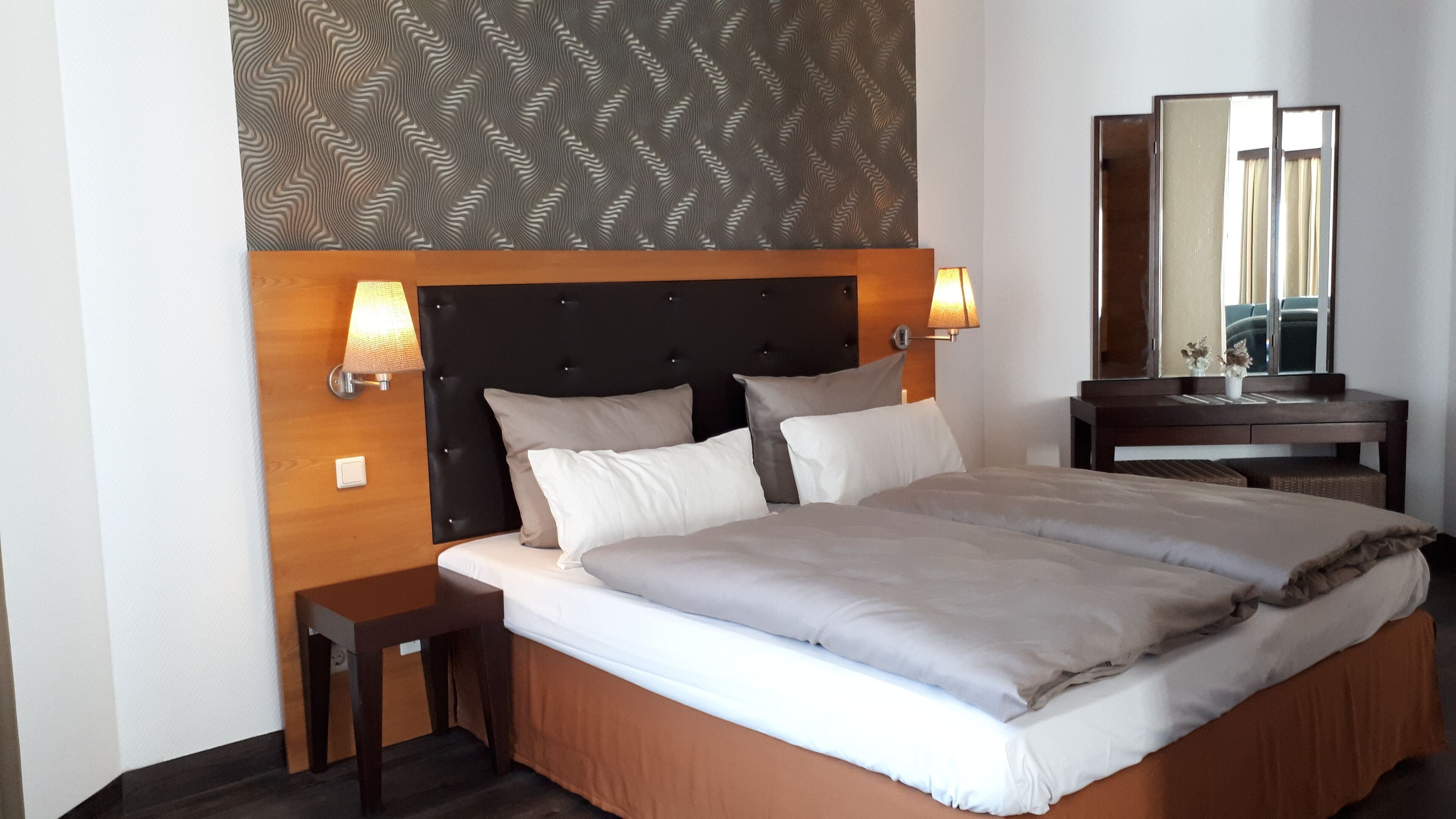A neatly made bed with a headboard, two bedside tables, a nightstand, and a mirror.