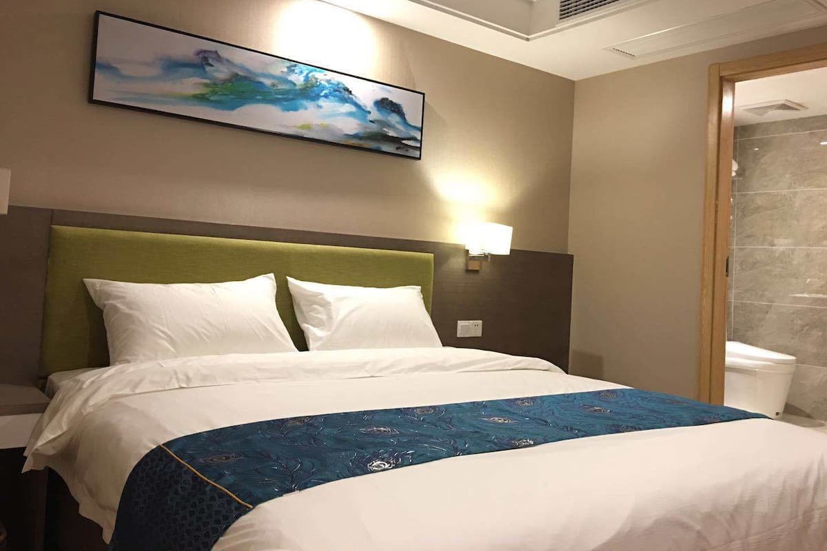 Une chambre d’hôtel avec un lit, un tableau, une table de chevet et une salle de bain visible à travers une porte ouverte.