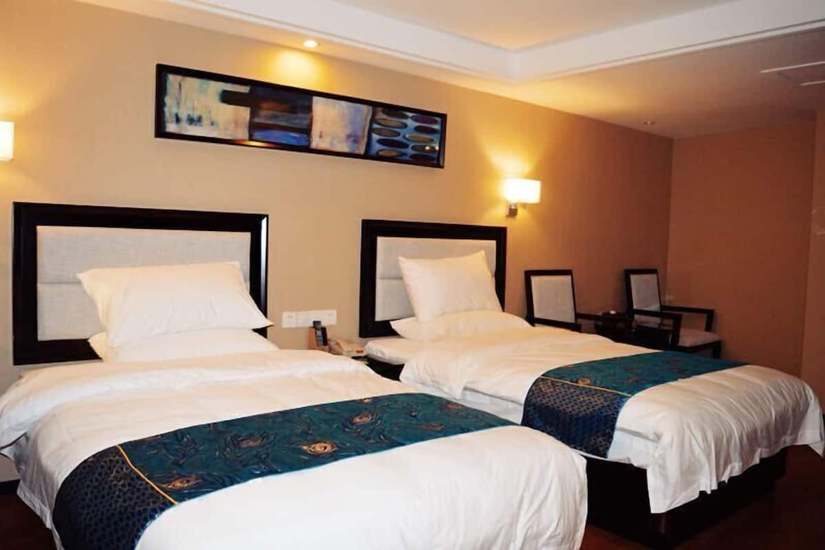 Une chambre d’hôtel avec deux lits, chacun doté d’une tête de lit et de tables de chevet. Un tableau est accroché au mur au-dessus des lits, et une lampe est fixée au mur, à droite.