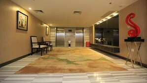 A hotel lobby with a patterned carpet, a reception desk, two chairs, a large red sculpture, and an elevator. - Shanshui Trends Hotel Pingtan Branch (Fuzhou)