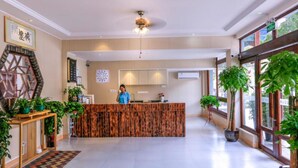 A reception area with a wooden reception desk, a ceiling fan, and potted plants. - Floral Hotel Libo Meet Inn (Qiannan)