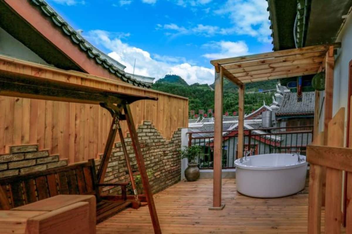 Una terraza de madera con un jacuzzi, un columpio de madera y un muro de piedra.