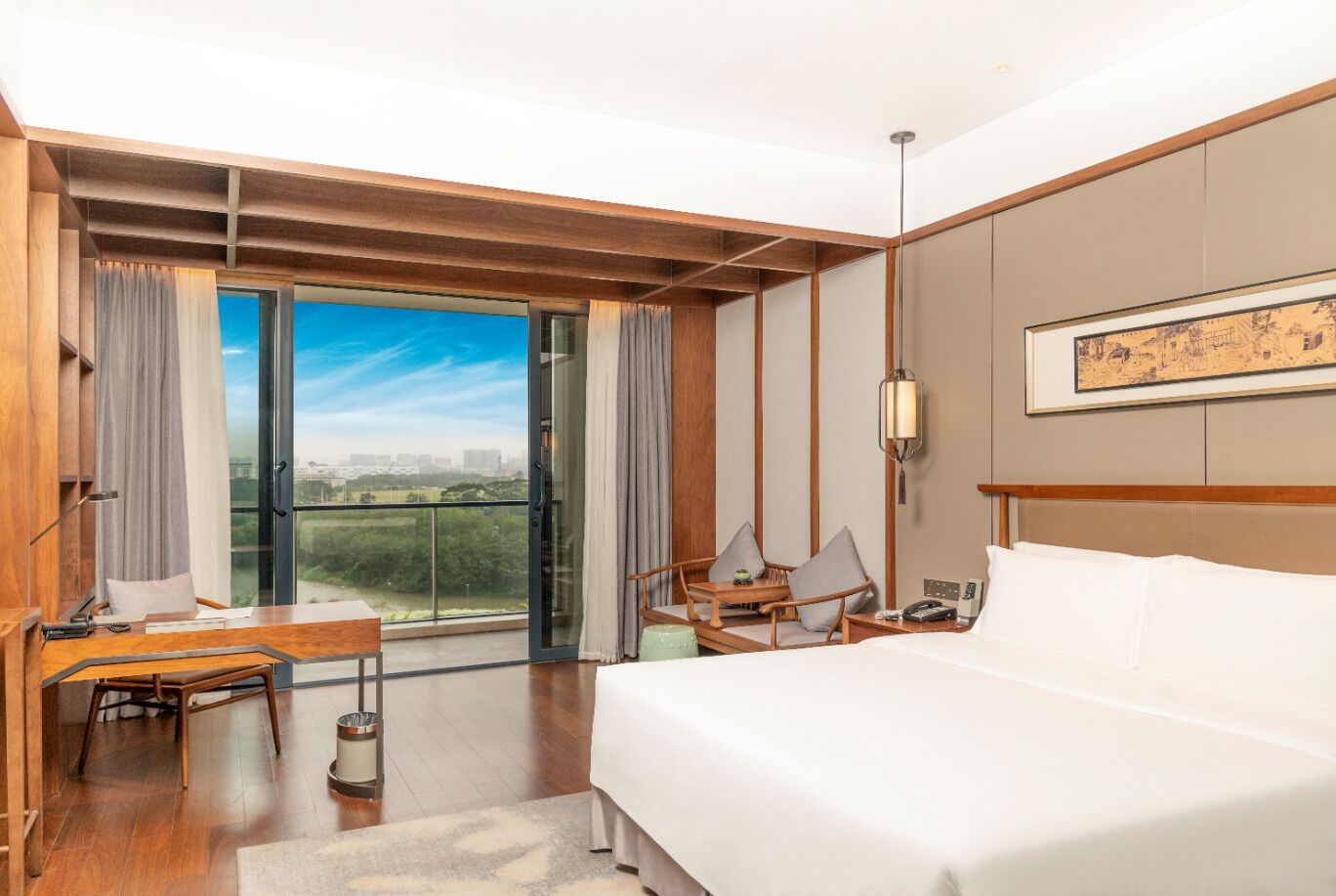 Habitación de hotel con una cama grande, un escritorio, una silla, un balcón con vistas y un cuadro en la pared.