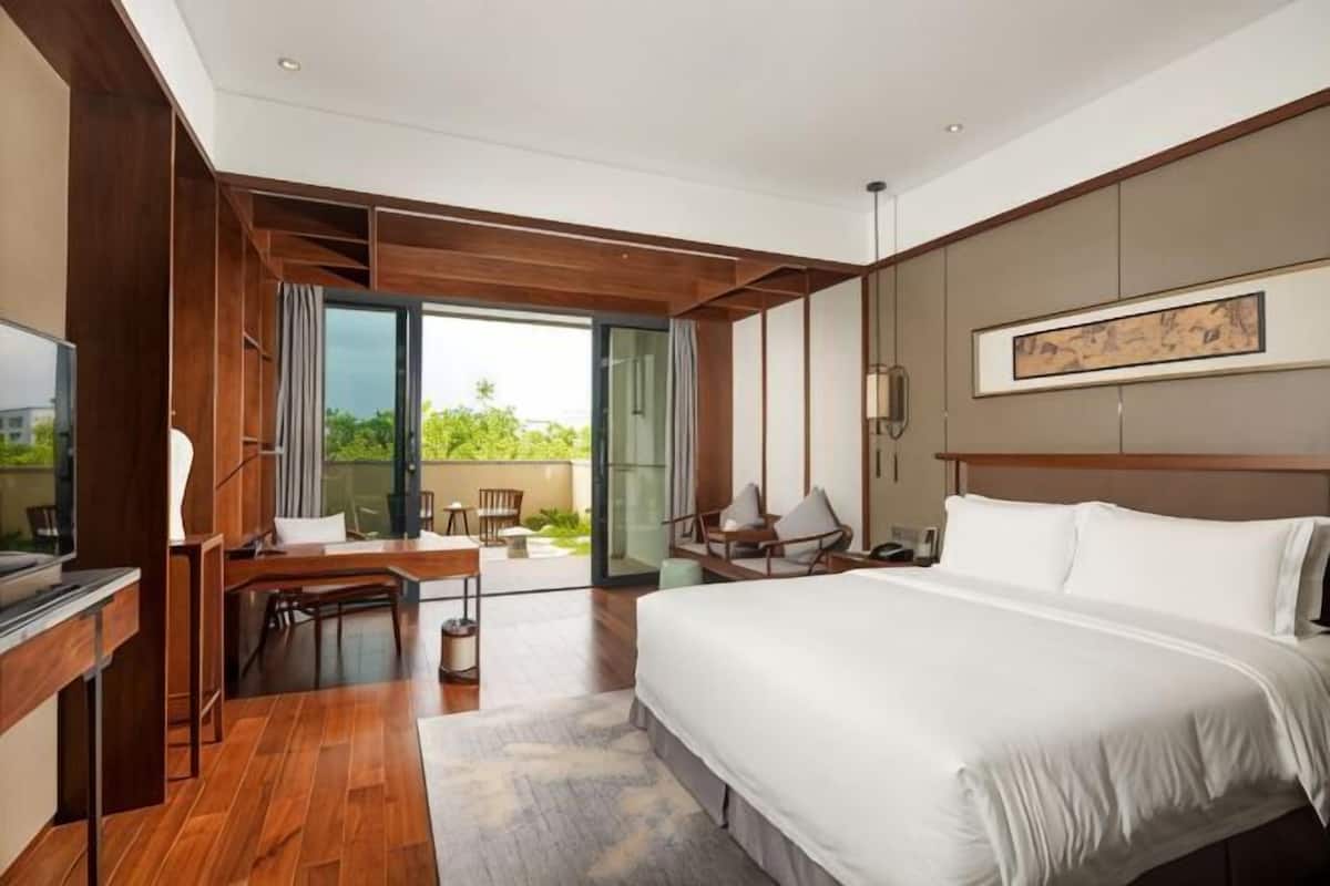 A hotel room with a bed, a desk, a television, and a balcony with a view.
