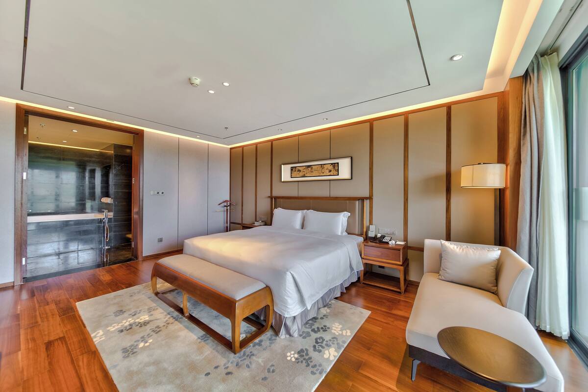 A modern bedroom with a large bed, a bench, a sofa, and a bedside table.