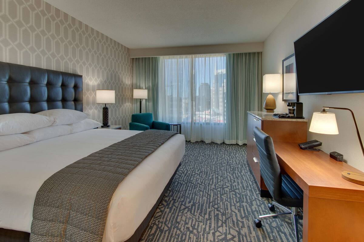 Une chambre d’hôtel avec un grand lit, un bureau avec une chaise, un téléviseur à écran plat et une fenêtre avec des rideaux.