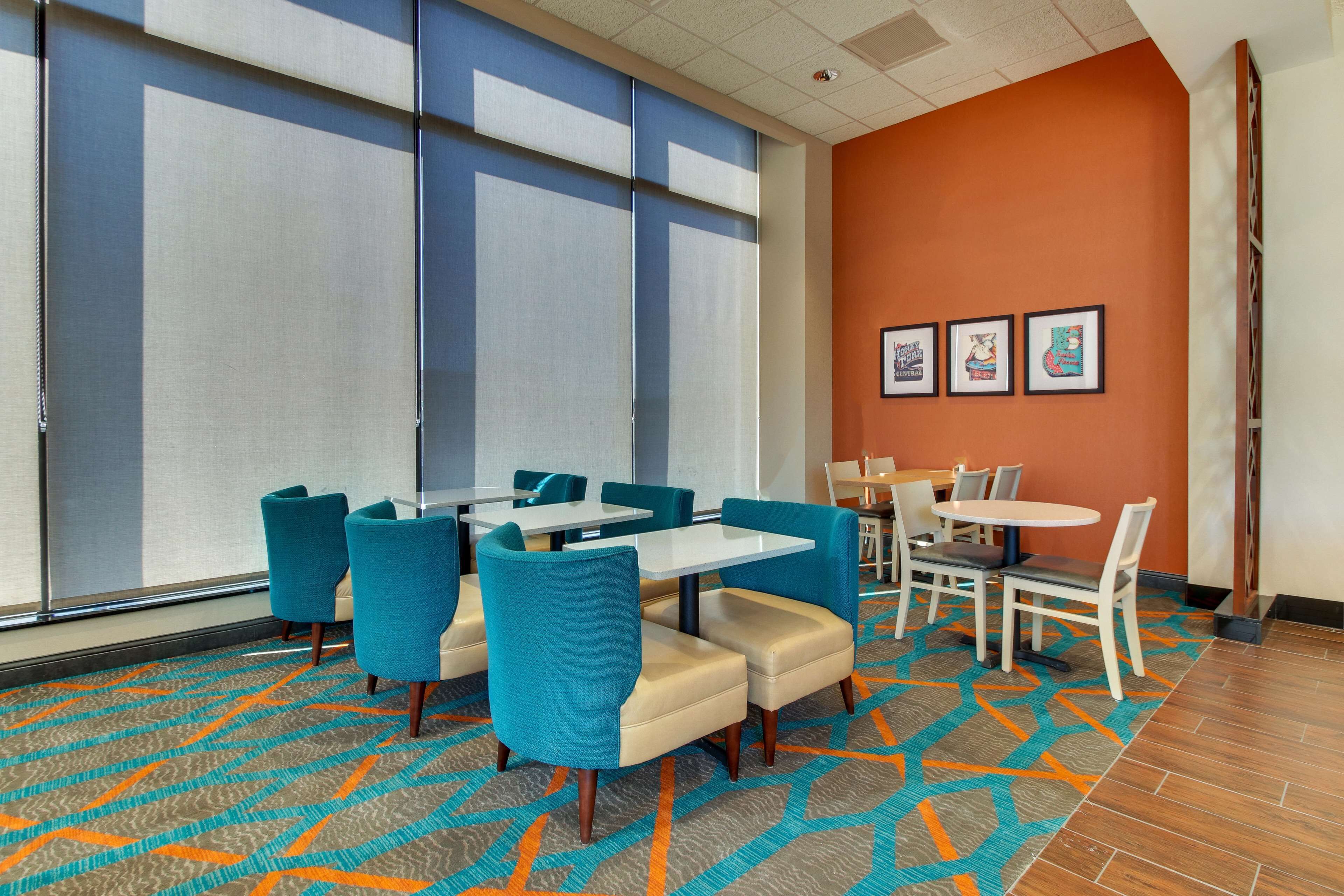 A hotel room with a large window, a patterned carpet, and a seating area with tables and chairs.