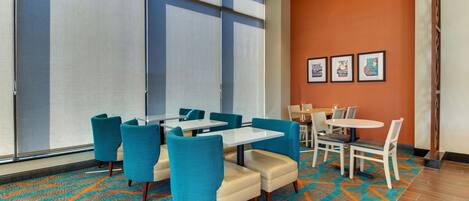 A hotel room with a large window, a patterned carpet, and a seating area with tables and chairs.