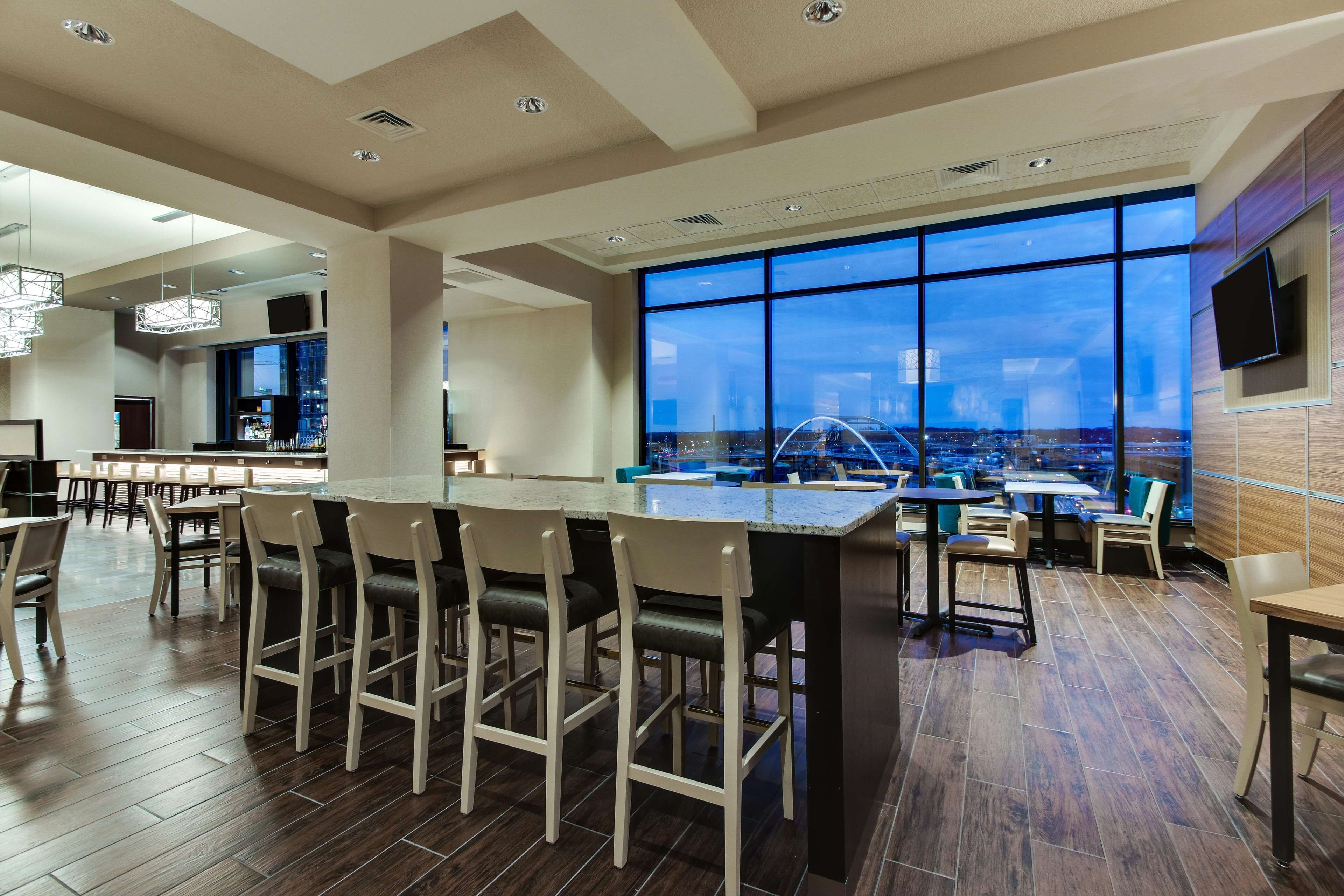 A modern bar area with a pool table, bar stools, and a large window offering a city view.