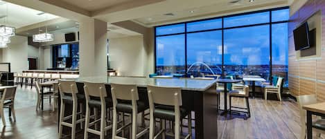 A modern bar area with a pool table, bar stools, and a large window offering a city view.