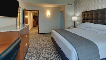 Habitación de hotel con cama, escritorio con televisor de pantalla plana, lámpara y alfombra estampada.