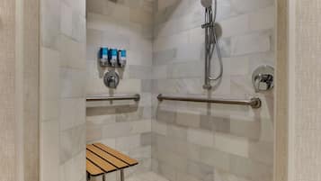 Douchegedeelte met witte marmertegels, een handdouche en een klein houten krukje.