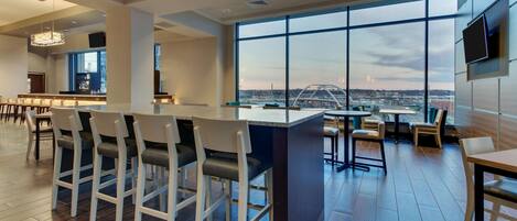 A modern bar area with high ceilings, large windows, and a city view.