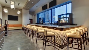 A modern bar area with a long counter, multiple stools, and a large window offering a city view. - Drury Plaza Hotel Nashville Downtown (Nashville)
