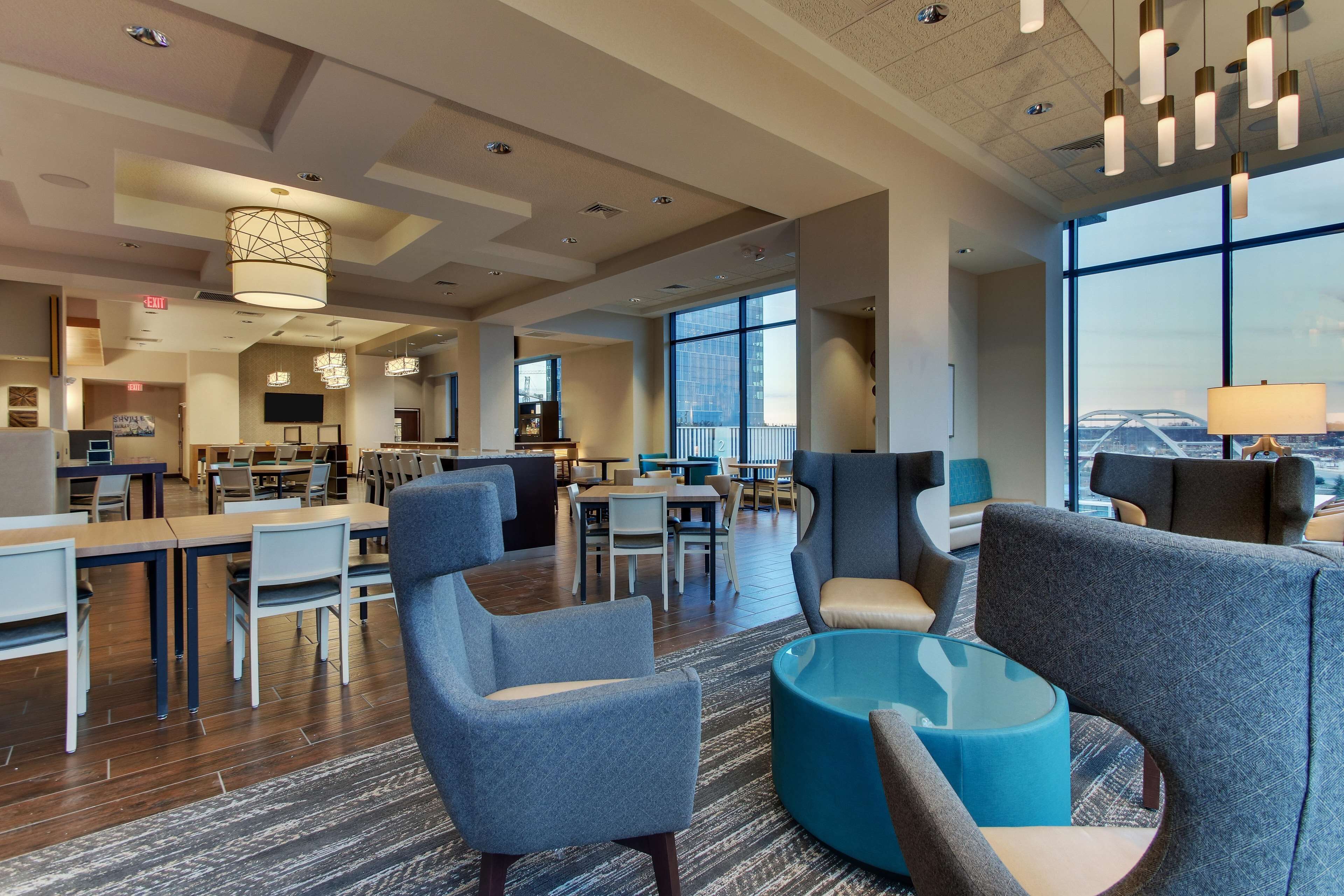 A spacious hotel lobby with modern furniture, large windows offering city views, and a variety of seating arrangements.