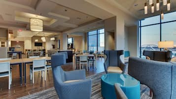 A spacious hotel lobby with modern furniture, large windows offering city views, and a variety of seating arrangements.
