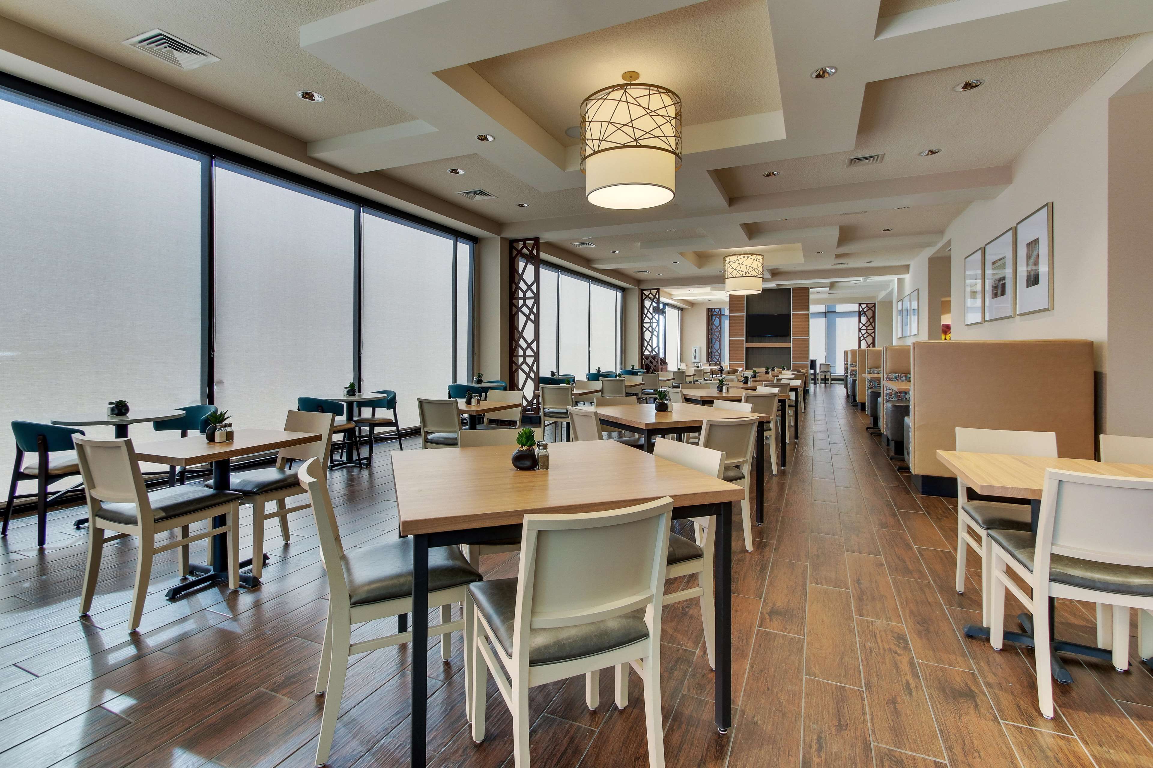 A spacious dining area with multiple tables and chairs, large windows, and modern lighting fixtures.