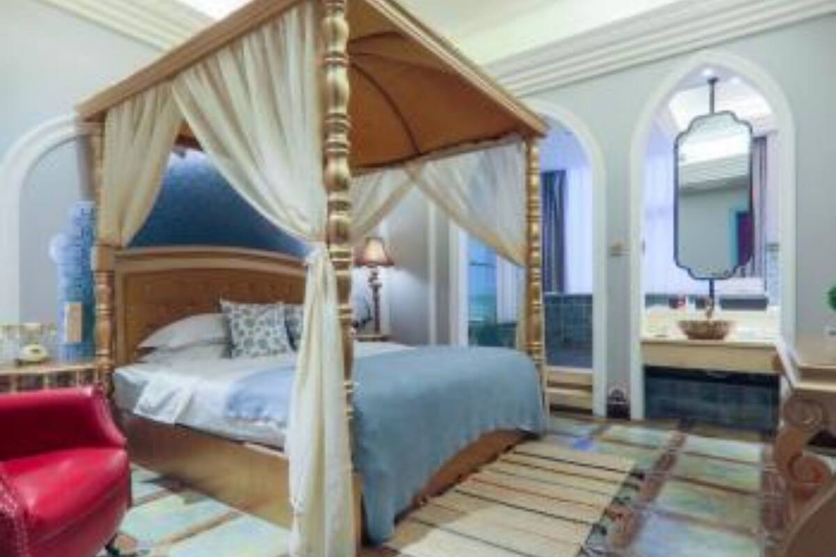 Una cama con dosel y cuatro columnas, cabecera de madera, un sillón rojo y suelo de baldosas.