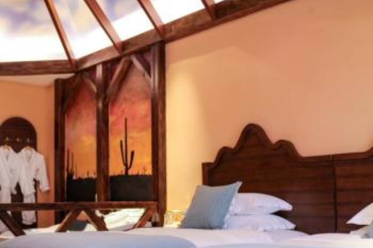 Una habitación con dos camas, cabeceros de madera y un cuadro grande con un paisaje desértico.