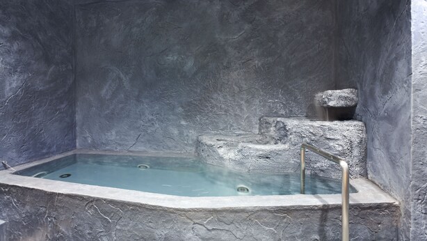 A stone bathtub with a metal ladder, set against a textured stone wall. - Yukkura Inn (Aizuwakamatsu)