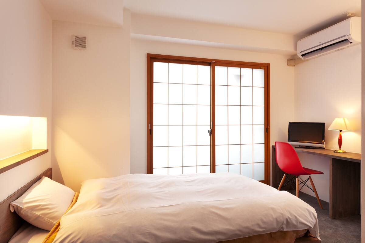 Een hotelkamer met een bed, een bureau met een computer, een rode stoel en een schuifdeur.