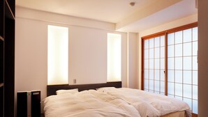 A bedroom with a large bed, a wooden headboard, and a sliding shoji screen door. - Yukkura Inn (Aizuwakamatsu)