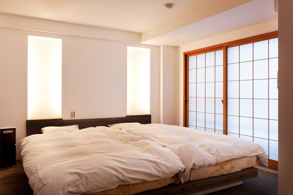 Een slaapkamer met een bed, twee nachtkastjes, een kledingkast met schuifdeur en een groot raam met uitzicht.