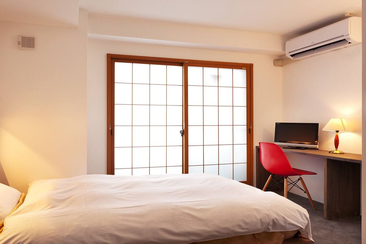 Een hotelkamer met een bed, een bureau met een computer, een rode stoel en een airconditioning.