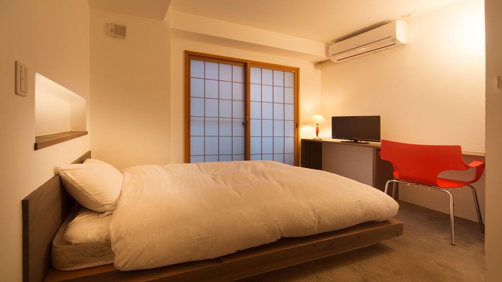 A bedroom with a bed, a TV, a chair, and a window with a view.