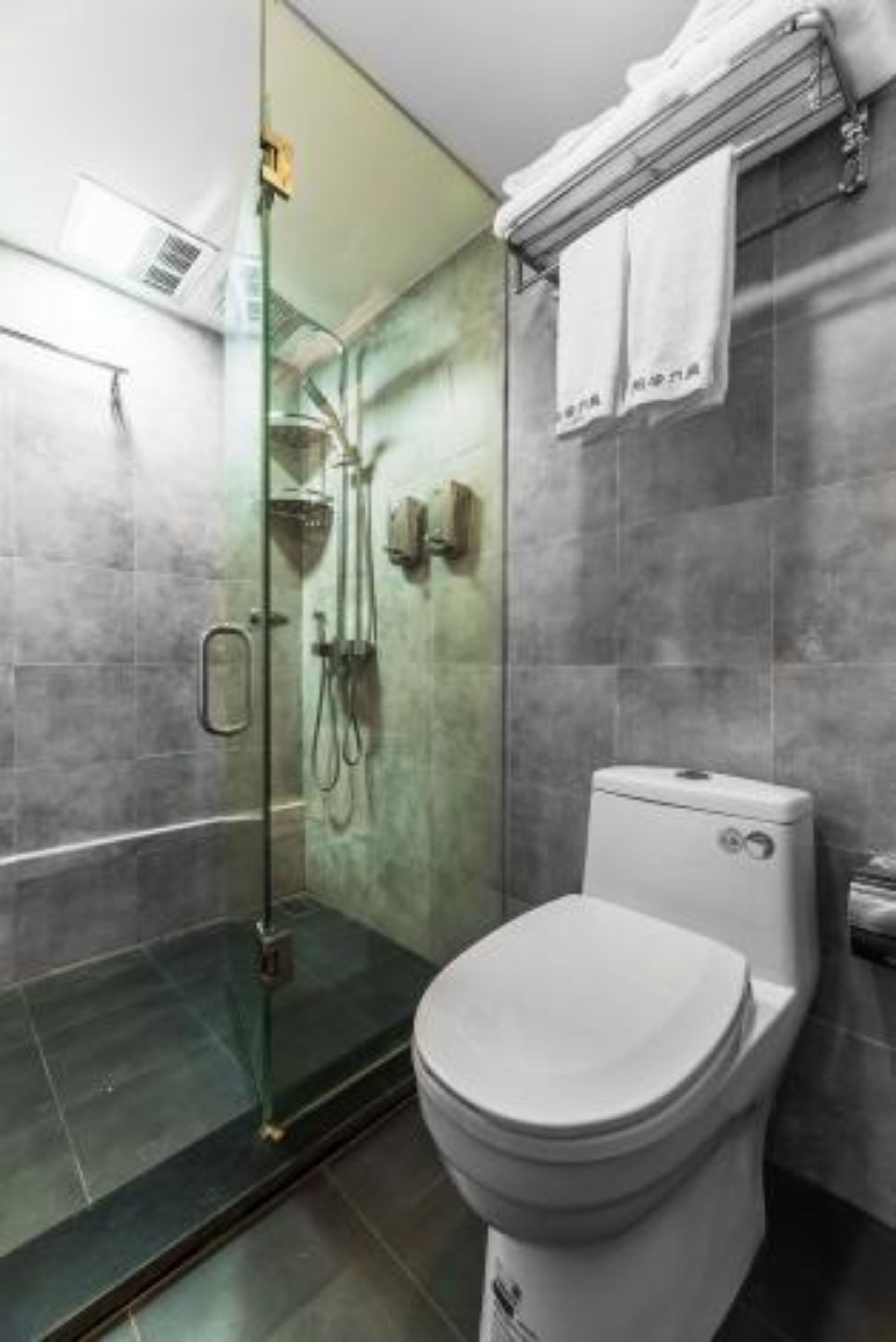 Une salle de bain moderne avec une douche à parois de verre, des toilettes blanches et un porte-serviettes avec deux serviettes.