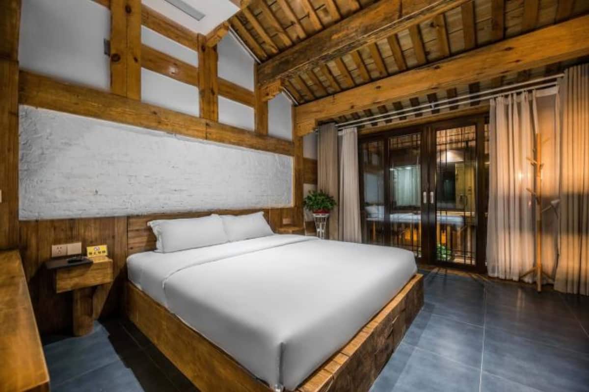 Ein Schlafzimmer mit einem Holzkopfteil, einem großen Bett, einem Nachttisch und Blick ins Freie durch eine Glastür.