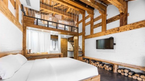 Ein Schlafzimmer mit einem Holzbettgestell, einem an der Wand befestigten Fernseher und einem Fenster mit Vorhängen.