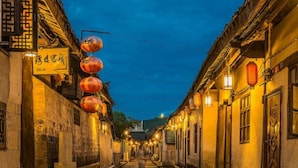 Eine schmale Gasse, gesäumt von traditionellen Gebäuden, beleuchtet von hängenden Laternen und Straßenlaternen.