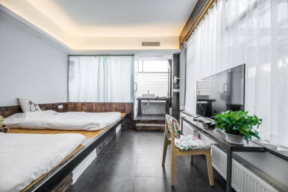 Ein Hotelzimmer mit zwei Betten, einem Schreibtisch, einem Sessel, einem Fernseher und einem Fenster mit Vorhängen.