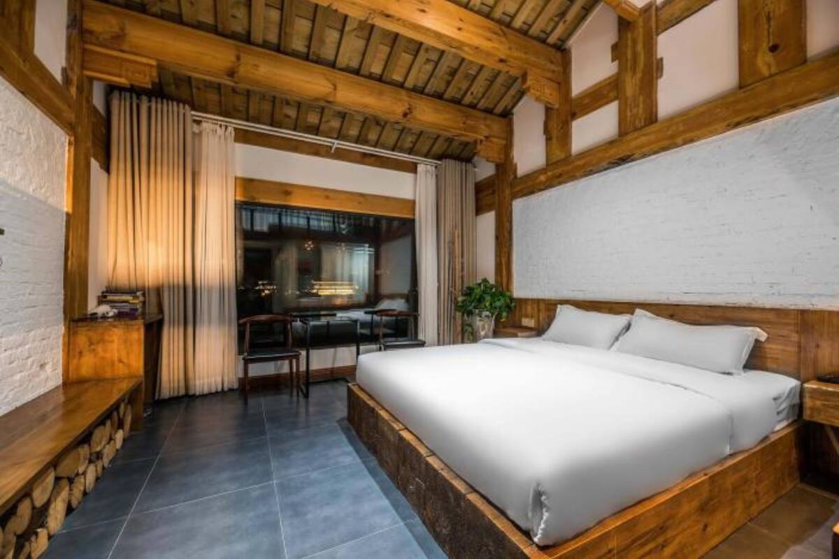 Ein Schlafzimmer mit einem großen Bett, Holzbalken, einem Schreibtisch und einem Fenster.