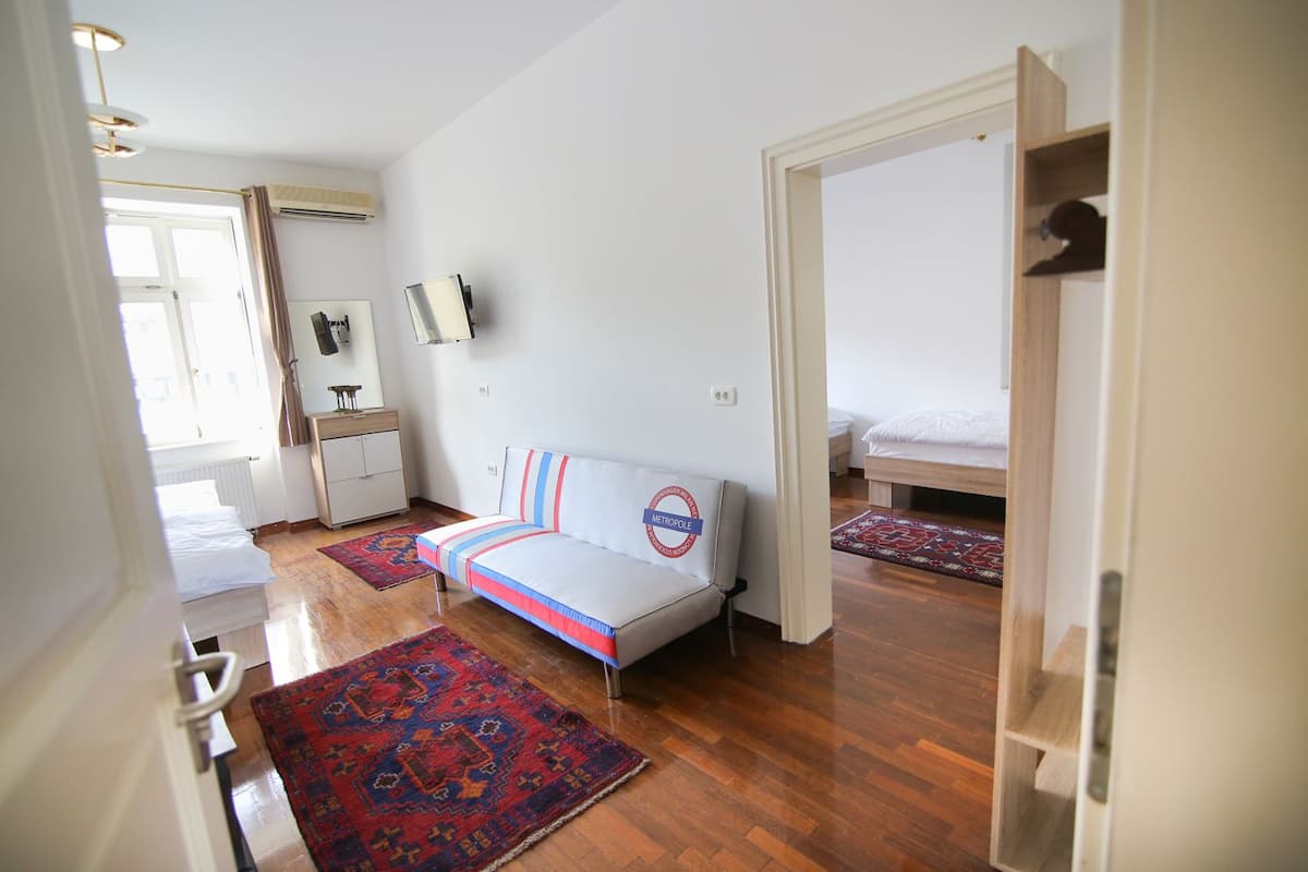 A bedroom with a sofa bed, a wooden floor, a red and blue rug, and a white door.